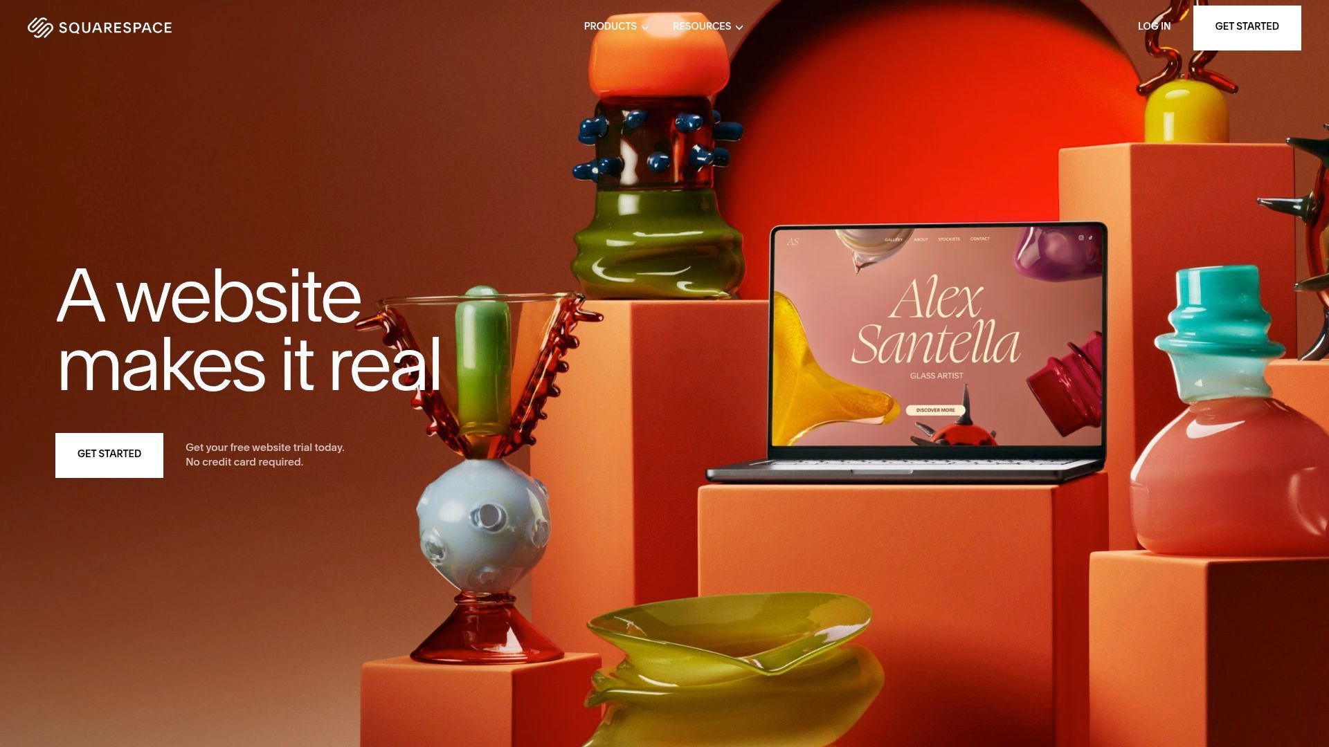 Orange still life with colorful sculptures and a laptop screen that displays 